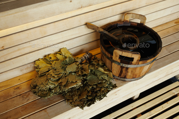 Sauna bucket full of water with ladle and broom on the wooden bench