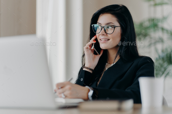 Elegant female entrepreneur with satisfied expression has telephone conversation