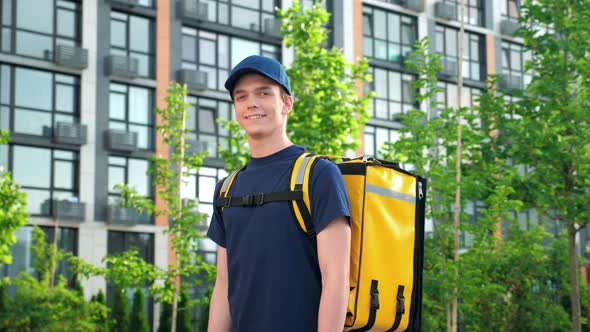 Positive Deliveryman Worker Wears Tshirt and Cap on Background Modern Building alt