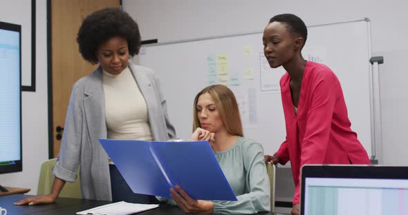 Three diverse businesswomen in discussion looking at paperwork in an office alt