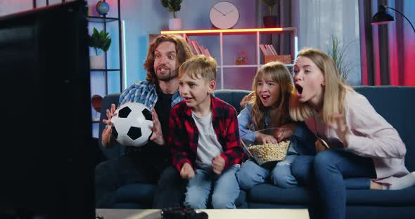 Football Fans Family Sitting in front of TV in the Evening and Rejoycing from Scored Goal alt