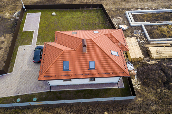 Aerial top view of house metal shingle roof with attic windows and black car on paved yard