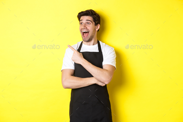 Waiter in black apron checking out promo offer, pointing finger and looking left at your logo
