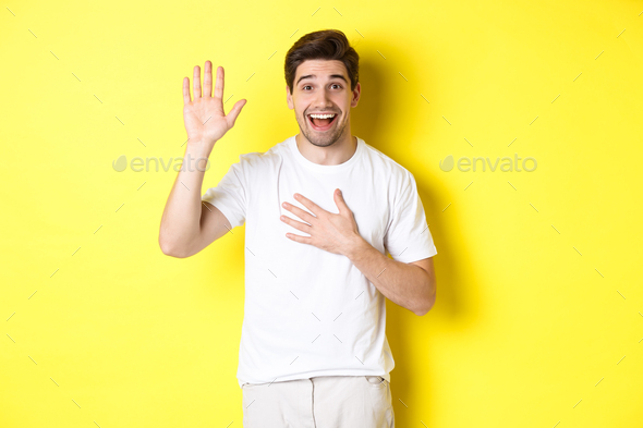 Happy guy making promise, holding hand on heart, swearing to tell truth, standing over yellow