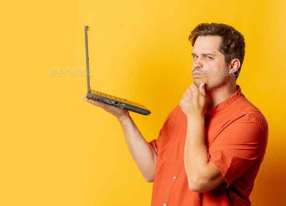 Stylish man in orange shirt with laptop computer on yellow background ...