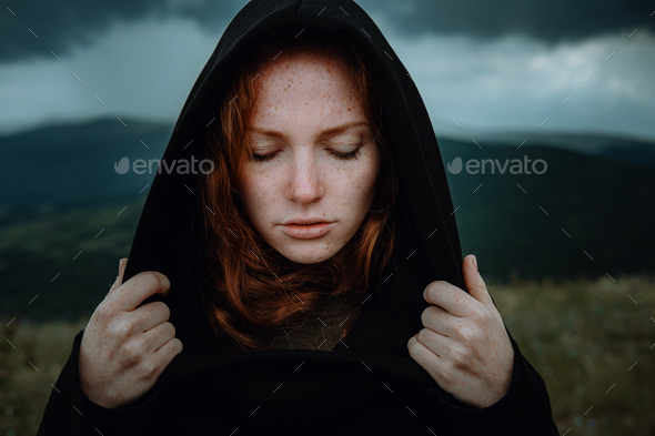 woman in black hood stands in the rain