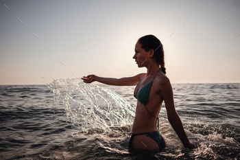 Beautiful Model Girl making splash in the sea at sunset