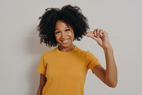 Cheerful smiling African American woman gestures small size with fingers