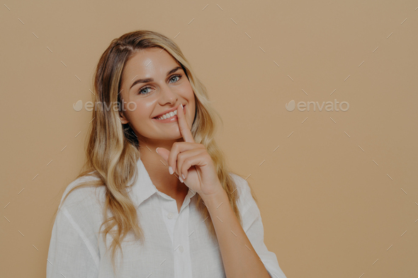 Beautiful young woman with long blonde dyed hair shows hush sign or keep silence gesture