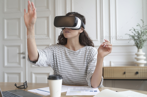 Concentrated woman bank accountant in VR headset sitting at desk at home office