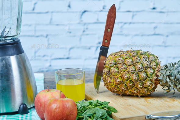 A pineapple, apple, berries, a glass of juice and teapot on blue background
