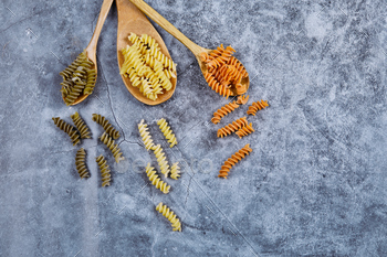 Raw fusilli and wooden spoons on blue background