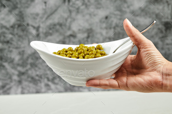 Hand holding a bowl of boiled green peas on a marble background