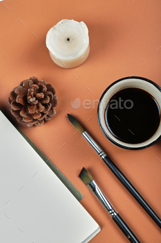 A cup of coffee with forest cone, candle, brushes on the orange background