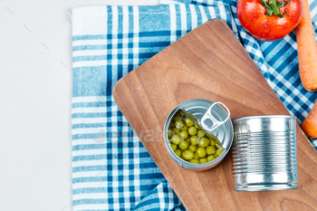 Two cans of boiled green peas, vegetables and tablecloth on a white background