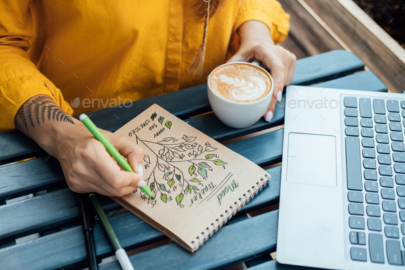Mental health mood tracker, Woman sitting in street cafe and fills mood tracker in notepad