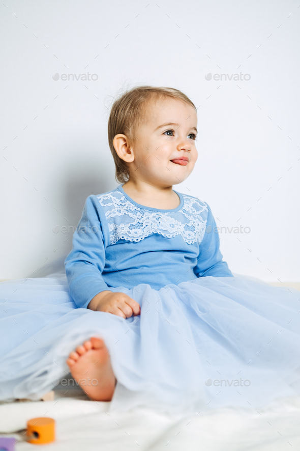 Cute baby girl in blue princess dress playing with toys at home. Stock Photo by IrynaKhabliuk