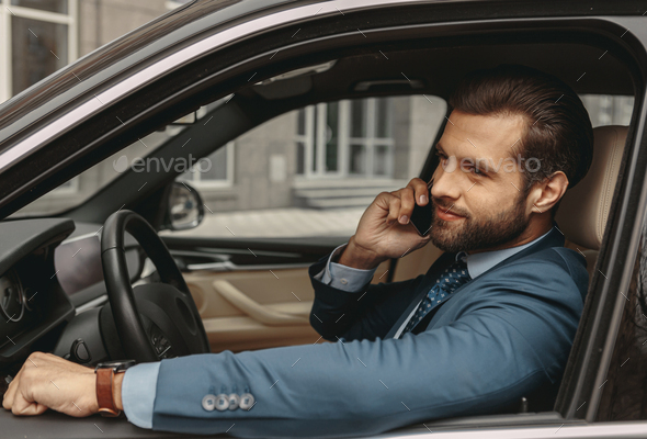 Adorable beaded businessman having conversation on smartphone in salon of automobile