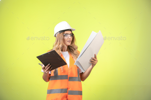 Female engineer in helmet and gear holding project plan and report list