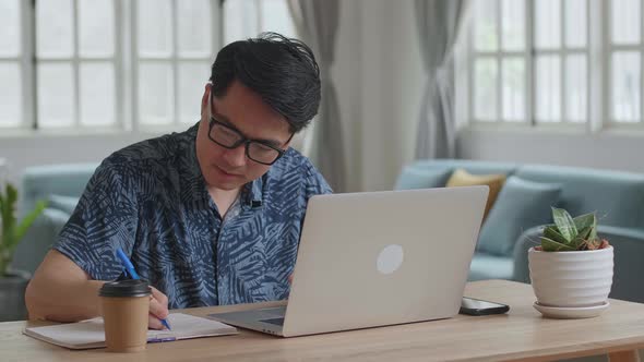 Asian Man Working With Laptop Computer And Writing On Notebook alt