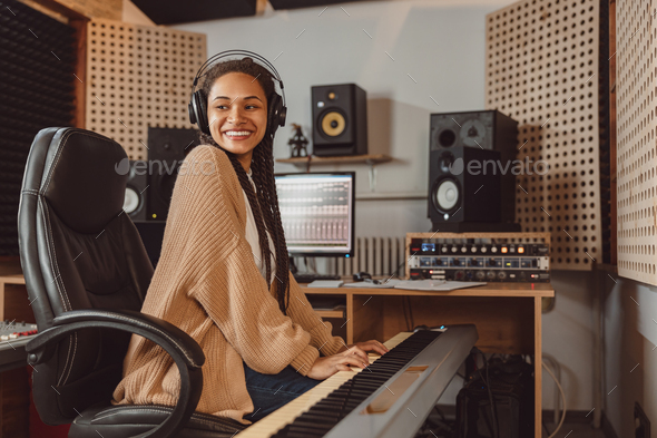 Attractive stylish African American female musician sound engineer playing synthesizer