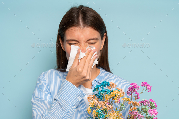 Portrait of woman with allergy on wild flowers pollen odor blowing runny nose in tissue after smell