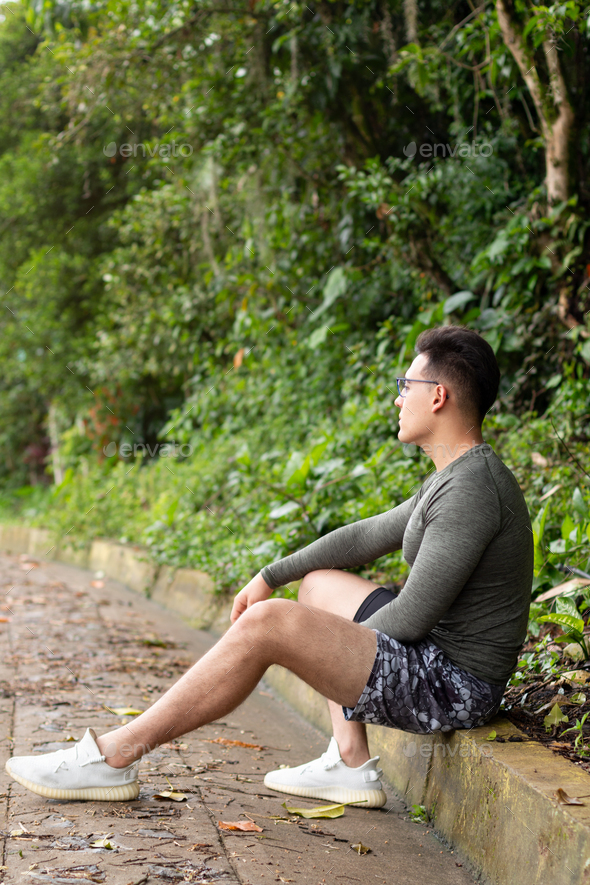 Vertical photo of athlete resting on the roadside. Seated young adult resting after exercise.