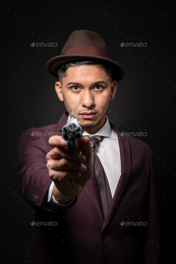 Latin man with suit and pistol on black background pointing at camera