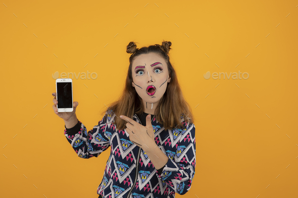 Portrait of shocked girl with creative makeup and point finger to her phone