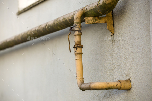 Close-up detail of old dirty painted yellow natural gas pipes with welding seams and faucet valve