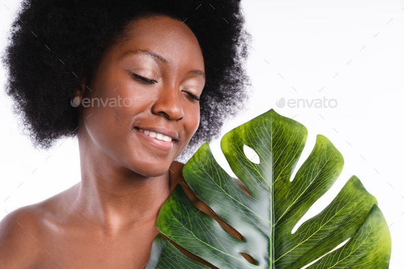 Close up shot of an african young girl shirtless holding tropical leaf isolated in white