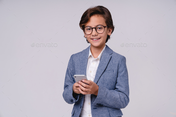 Cheerful little boy in formal attire using mobile phone isolated over grey background - Stock Photo - Images