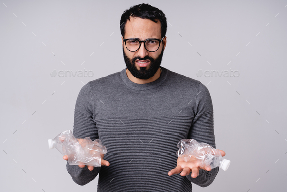 Disappointed young Arabic man holding plastic bottles isolated over grey background