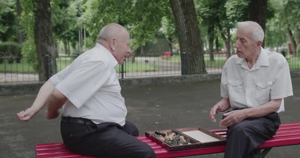 Two Seniors Men Play Entertaining Games on Bench Outdoors in Summer alt