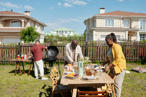 Young black man and woman serving table with homemade food and drinks