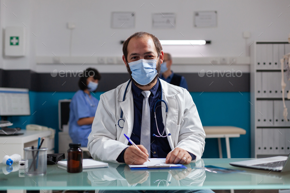 Portrait of physician with white coat and face mask in office