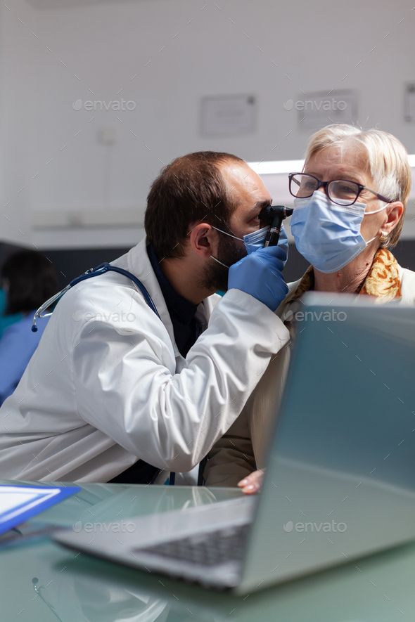 Specialist holding otoscope to do ear examination on senior woman