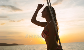 Sexy Asian woman in colorful bikini and sunglasses standing, looking away and enjoying sunset