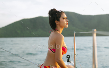 Asian woman in colorful bikini sit and relaxing at luxury yacht and looking for the sea.