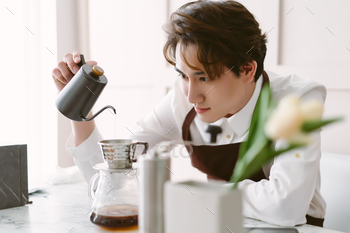 Asian barista man wearing apron preparing coffee using pour over coffee maker and drip in cafe