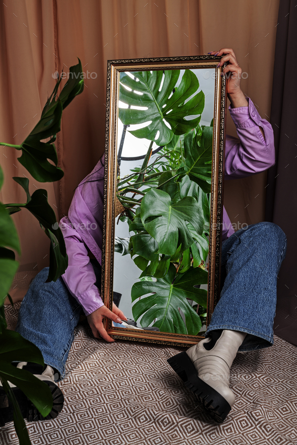 Jungles in the mirror. Woman holds mirror reflecting home jungles.