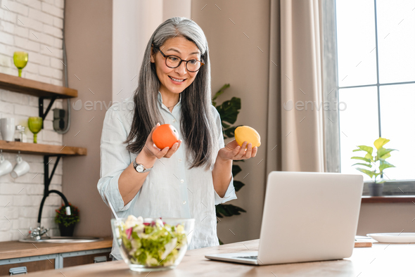 Mature pretty grey-haired woman recording her food blog in the kitchen