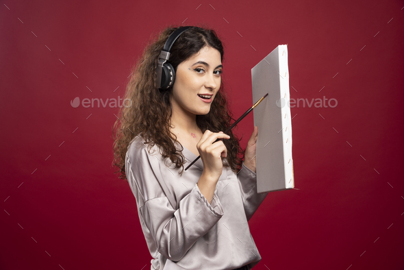 Woman in headphones painting on canvas over red background