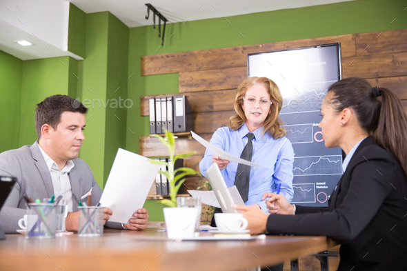 Executive female giving her assistant charts in a conference room