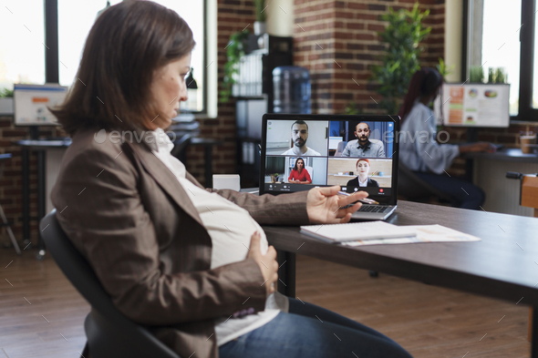 Pregnant woman on virtual conference videocall communicating marketing strategy to company partners.