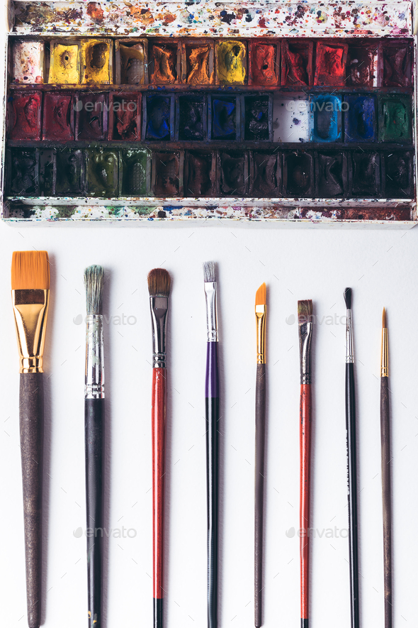 top view of well ordered paintbrushes and watercolour paints at designer workplace