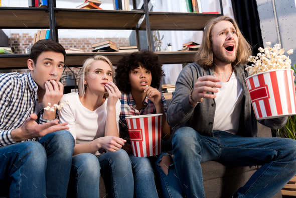 Shocked multicultural friends watching film with popcorn