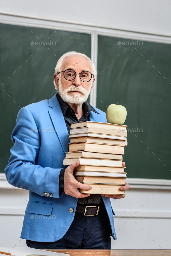 grey hair professor holding stack of books with apple on top