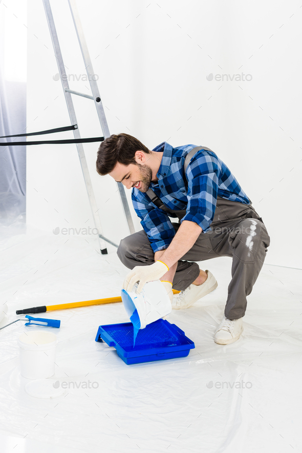 smiling man pouring paint from bucket into plastic paint tray