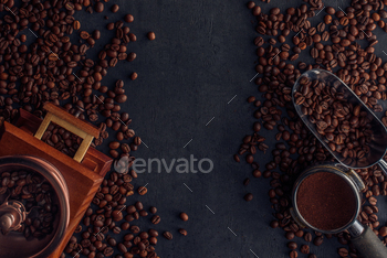 top view of roasted coffee beans, coffee grinder and scoop on black